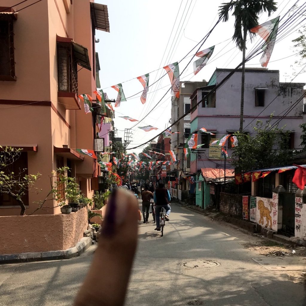 Image of inked finger (signifying voting) in front political banners in Kolkata